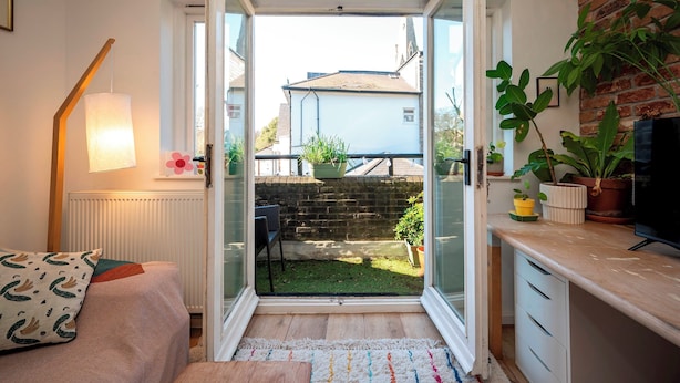A room with a sliding glass door leading to a backyard, a small seating area, and a TV on a wooden stand. - Artist's apartment in St Johns - Pass the Keys (London)