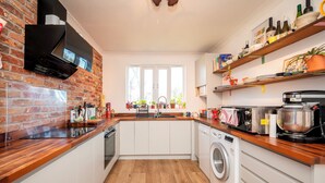 A kitchen with a brick wall, wooden countertop, white cabinets, a washing machine, and a window with plants. - Artist's apartment in St Johns - Pass the Keys (London)