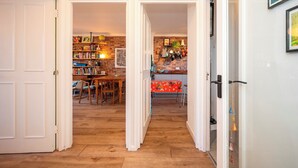 A hallway with a wooden floor, white walls, and a yellow ceiling. There are doors leading to different rooms, one with a red tablecloth and another with a brick wall and shelves. - Artist's apartment in St Johns - Pass the Keys (London)