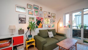 A living room with a green sofa, a small wooden table, a colorful rug, a bookshelf with red and white sections, and a variety of framed artworks on the wall. - Artist's apartment in St Johns - Pass the Keys (London)