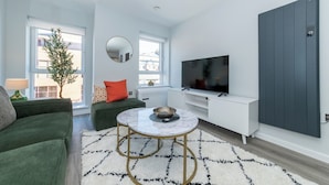 A modern living room with a sofa, a coffee table, a TV, and a large window. - Brand New Flat with AC 5-Min Walk to Town Centre - Pass the Keys (Reading)