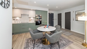 A modern kitchen with a round dining table, grey chairs, and a patterned rug. - Brand New Flat with AC 5-Min Walk to Town Centre - Pass the Keys (Reading)