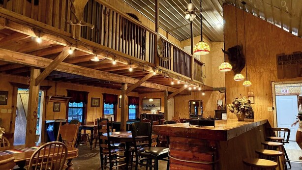 A rustic interior with wooden beams, a bar area, and multiple seating options. - Step Into Your Own Western Town Cabins, Saloon, ATV Trails & Private Group Stays (Winfield)