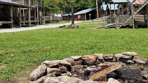 A rustic wooden building with a porch and a stone wall in the foreground. - Step Into Your Own Western Town Cabins, Saloon, ATV Trails & Private Group Stays (Winfield)