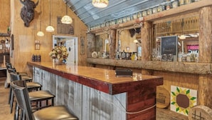 A rustic bar area with wooden decor, a counter, and bar stools. - Step Into Your Own Western Town Cabins, Saloon, ATV Trails & Private Group Stays (Winfield)