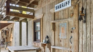 A rustic wooden building with a 'SHERIFF' sign, a table, chairs, and a lantern. - Step Into Your Own Western Town Cabins, Saloon, ATV Trails & Private Group Stays (Winfield)