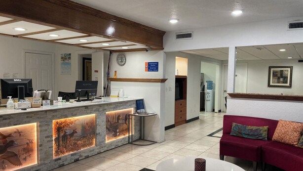 Ein Hotel-Rezeptionsbereich mit Theke, Computern, einer Uhr, einem Wasserspender und einem roten Sofa.
