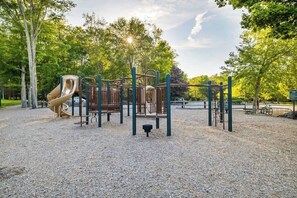 Un terrain de jeux avec un toboggan et des structures d’escalade, entouré d’arbres et recouvert de gravier.