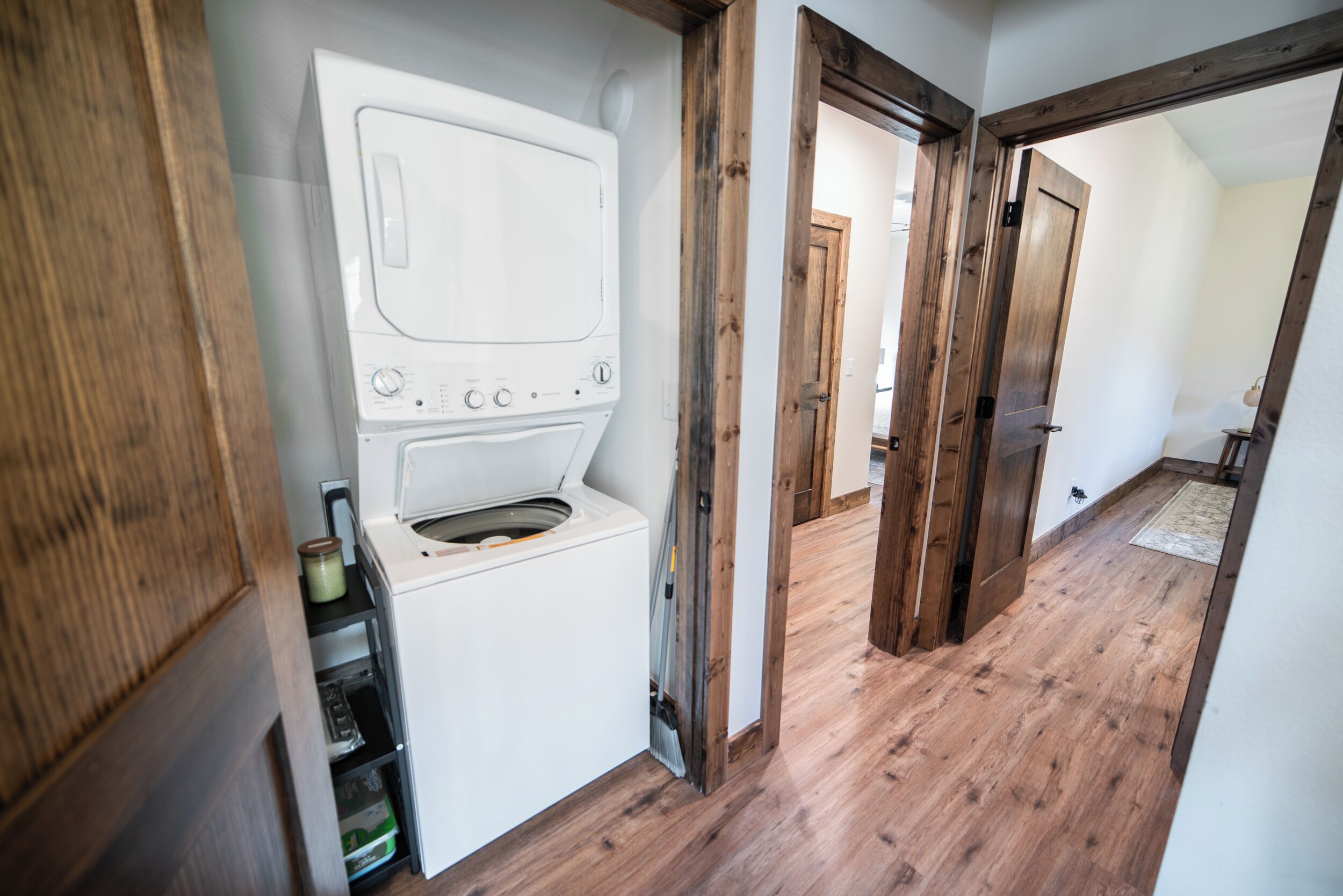 Een wasruimte met een wasmachine en droger, houten vloeren en openslaande deuren naar andere kamers.