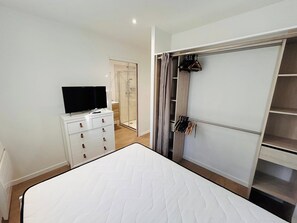 A bedroom with a bed, a TV on a dresser, a walk-in closet, and a shower. - La cour Bailla | Maison | Terrasse (Reims)