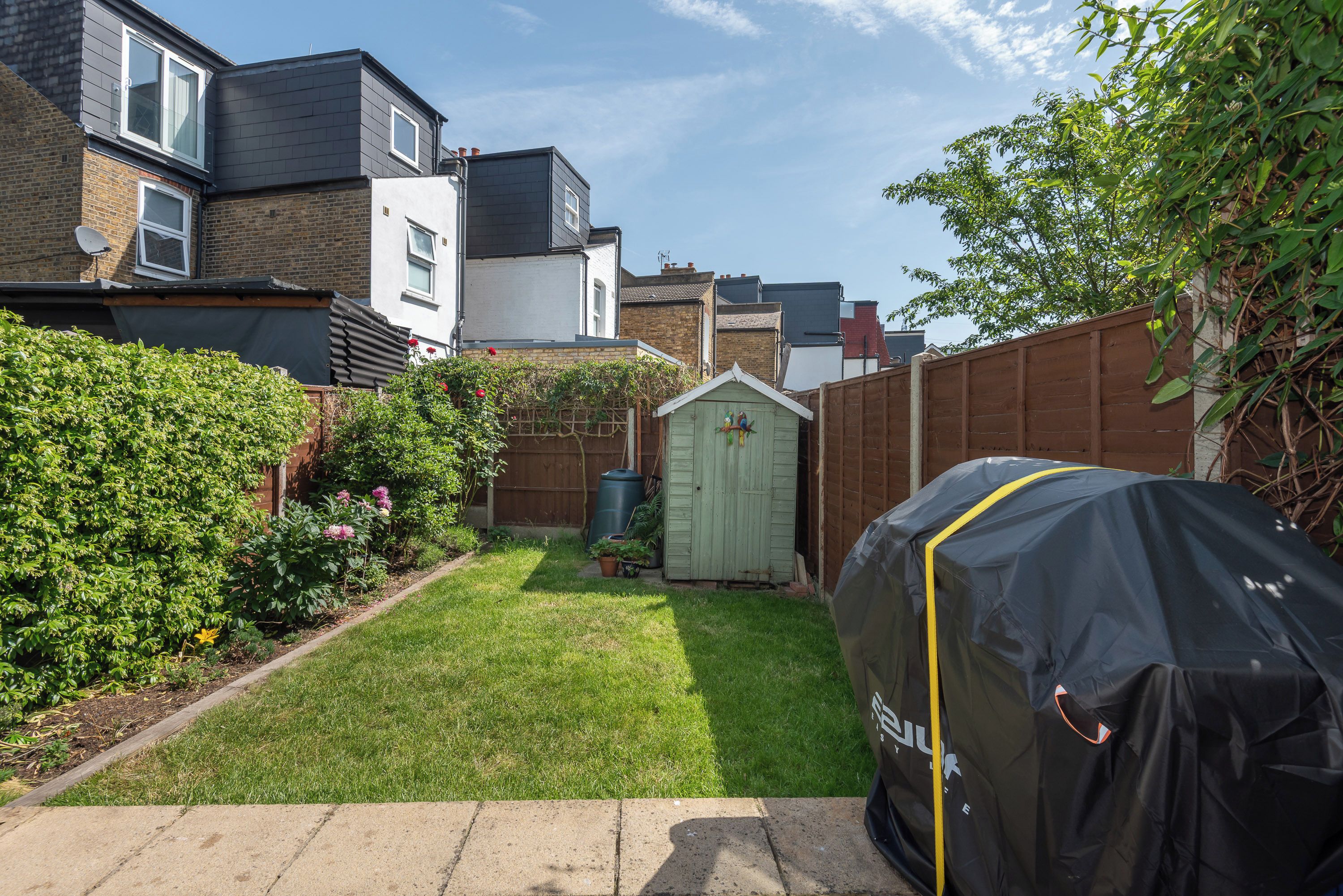 A residential backyard with a lawn, a wooden shed, and a barbecue grill covered with a protective sheet.