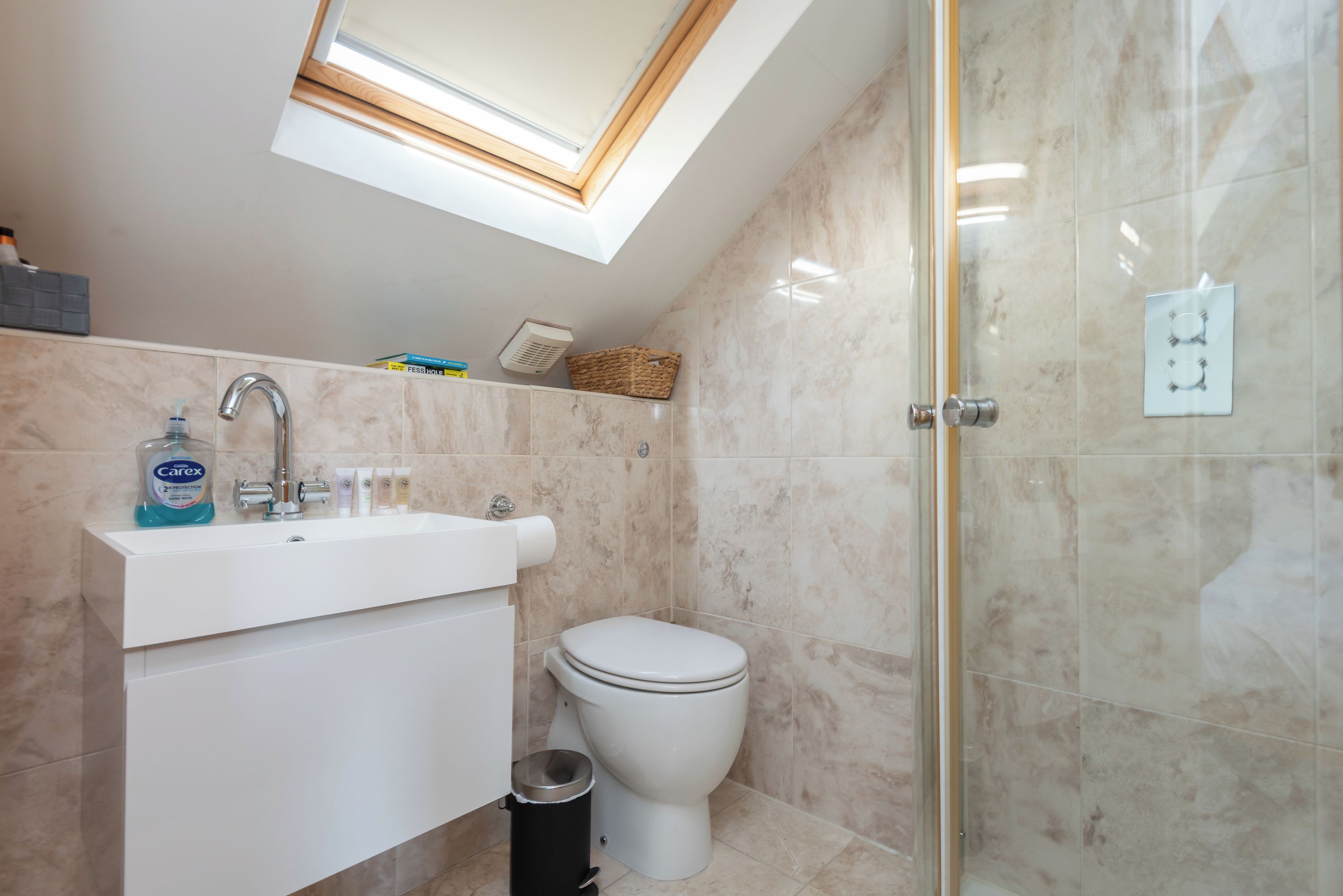 A bathroom with a skylight, a white sink, a toilet, and a glass shower enclosure.