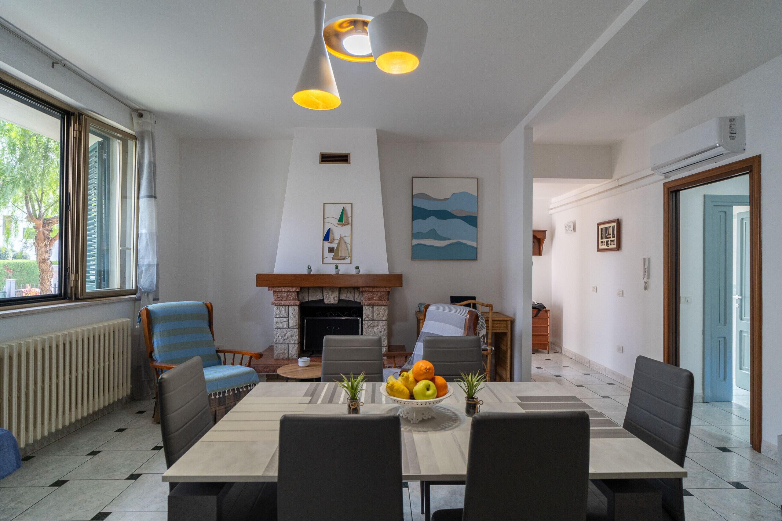 A dining area with a fireplace, a table with fruit, and a view of the outdoors.