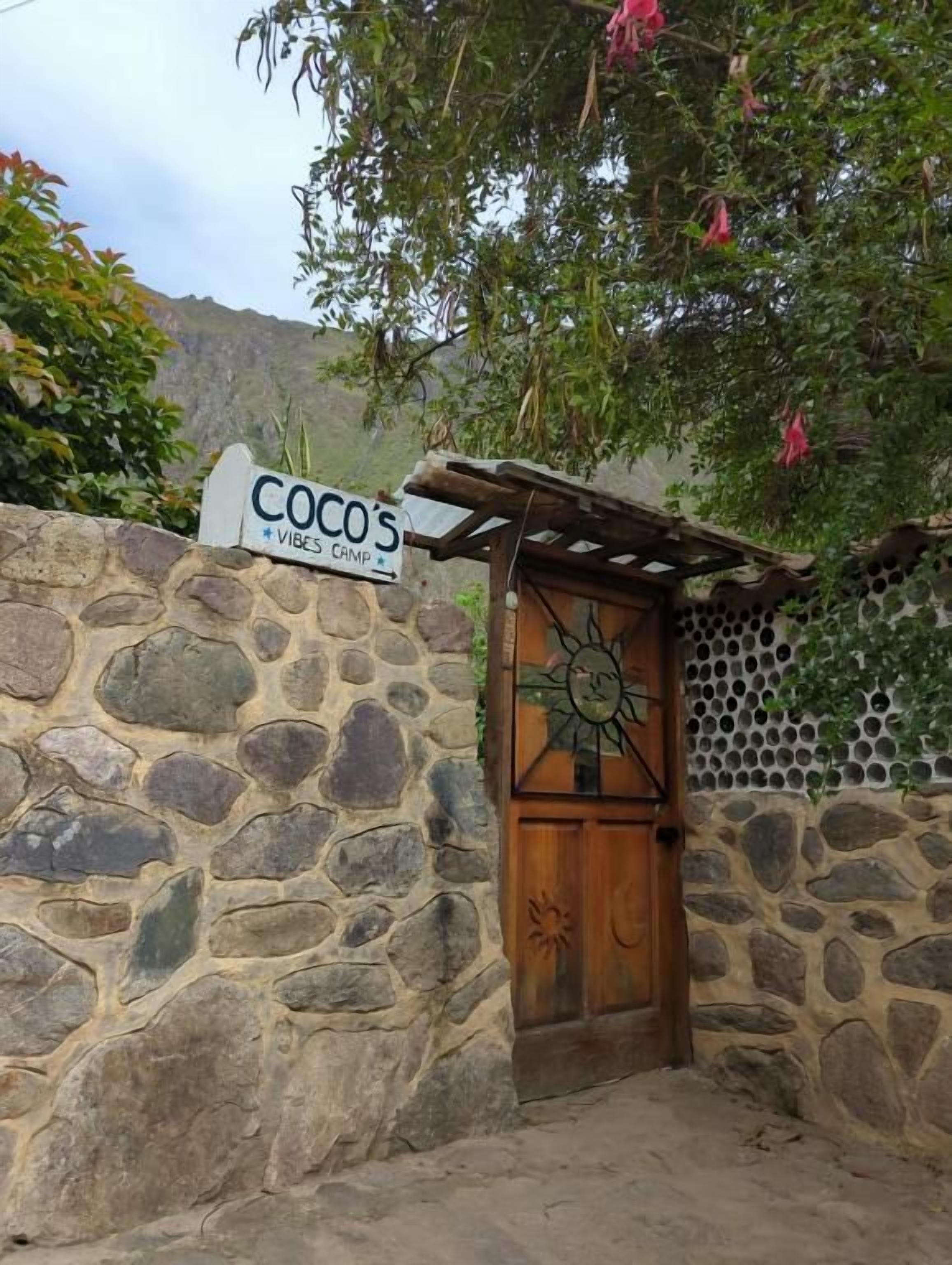 Eine Steinsäule mit einer Holztür und einem Schild, auf dem 'COCO'S VIBES CAMP' steht.