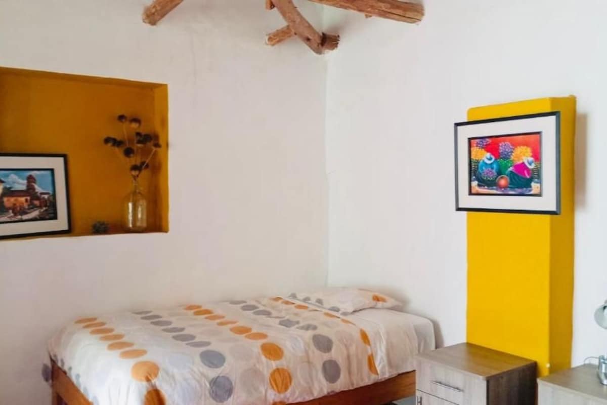Une chambre à coucher avec un lit, un petit bureau, une chaise et deux tableaux encadrés accrochés aux murs.