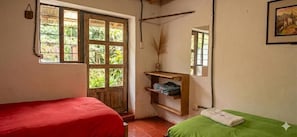 Une chambre avec deux lits, une fenêtre donnant sur un paysage verdoyant, une étagère avec quelques objets et un tableau encadré au mur.