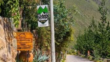 A paved road with a stone wall and a flagpole with a red flag and a rainbow flag. There are signs indicating a mountain and a lodge.