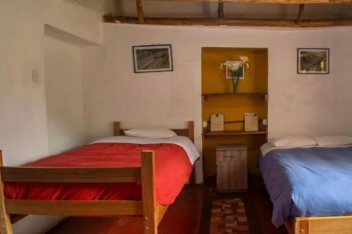 Une petite pièce agréable, dotée de deux lits en bois, d’une étagère avec un vase et d’une fenêtre avec un rideau.