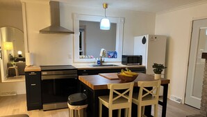 Et moderne køkken med en central ø, rustfrie hvidevarer og kig til opholdsstuen.