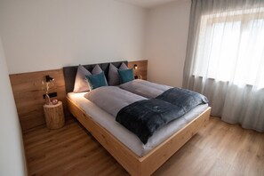 A modern bedroom with a wooden bed frame, a nightstand, and a wall-mounted lamp. - Kerschbama Farm Apartment Peppe with Mountain View, Shared Garden and Wi-Fi (Valdaora di Sotto)