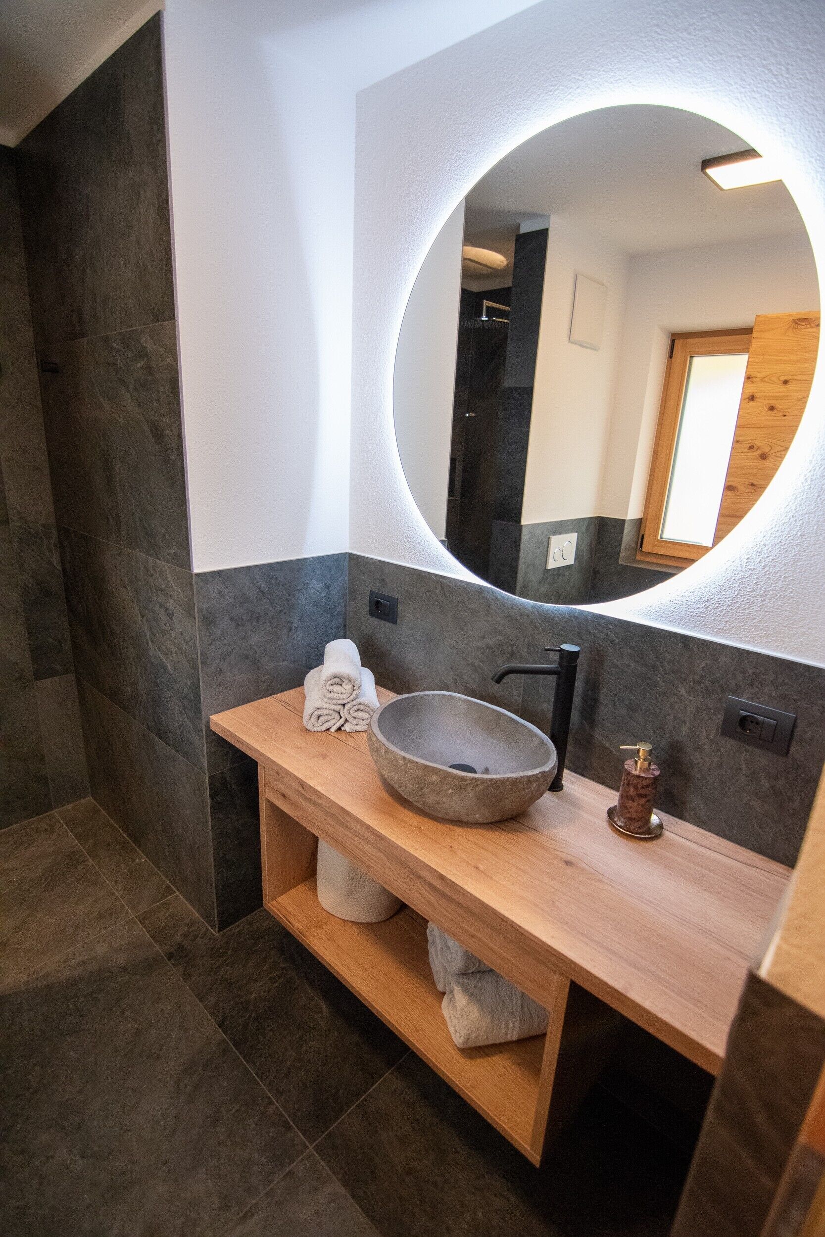 Een moderne badkamer met een stenen wastafel, een houten wastafelmeubel en een grote spiegel.