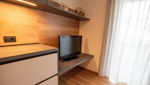 Une cuisine moderne dotée d’un téléviseur encastré, de meubles en bois et d’une fenêtre ornée de rideaux légers.