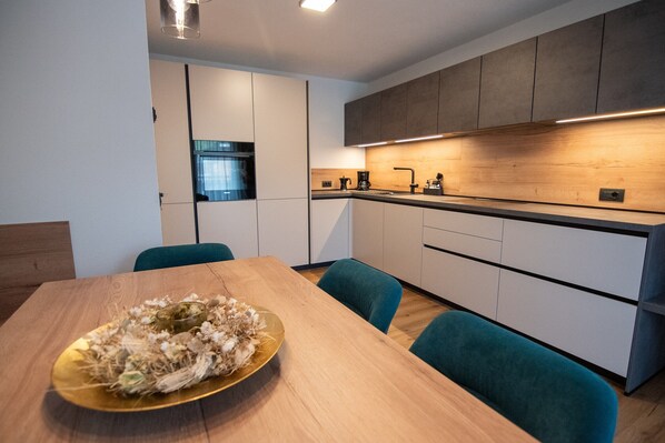 A modern kitchen with a wooden countertop, a sink, and a coffee maker. There is a dining table with chairs and a decorative centerpiece.