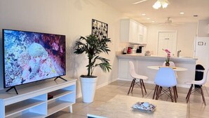 En moderne stue med et fladskærms-tv, et sofabord og et spiseområde med stole.