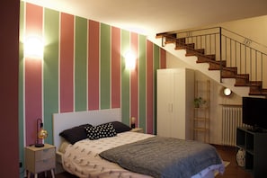 A bedroom with a bed, a nightstand, a lamp, a dresser, a TV, a staircase, and a radiator. - Tuscan Sunrise - Authentic Panoramic View (Uopini)