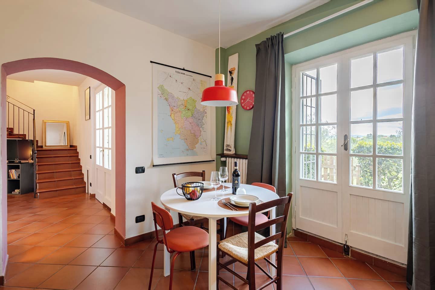 A dining area with a table set for two, a map on the wall, and a view through a window.