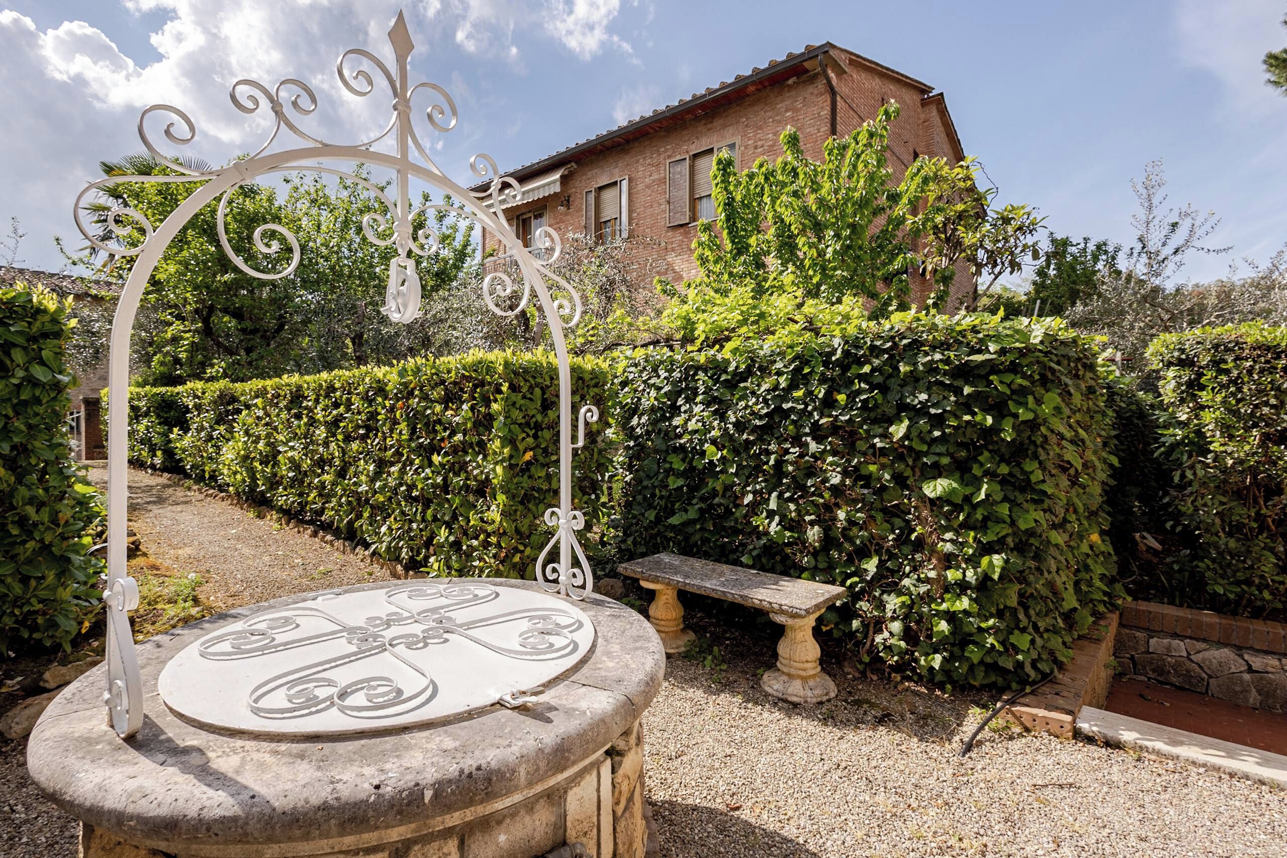 Ein Garten mit einer Steinsitzbank, einem Zierbogen aus Metall und einer Hecke.
