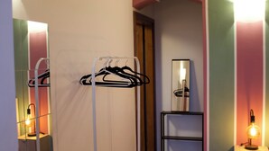 Habitació d'hotel amb mirall, un penjador, una taula petita amb una làmpada i un cistellera.