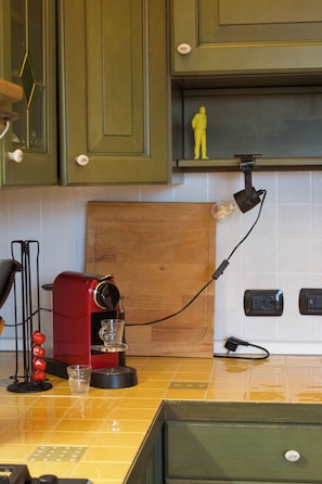 A kitchen with green cabinets, a red coffee maker, a wooden cutting board, and a light bulb on the wall. - Tuscan Sunrise - Authentic Panoramic View (Uopini)