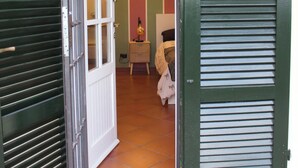 Una porta oberta que dona a una habitació amb un llit, una taula de nit i una làmpada.