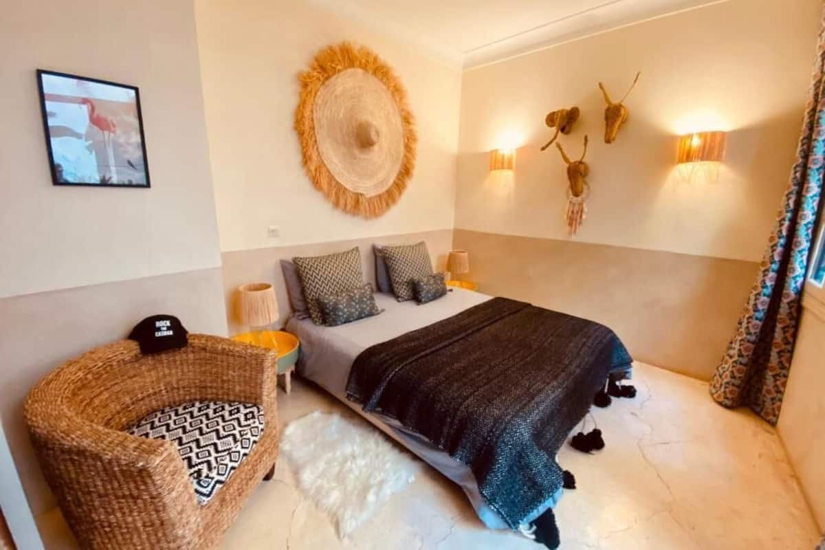 A bedroom with a bed, a woven basket, wall-mounted lights, and a framed picture.