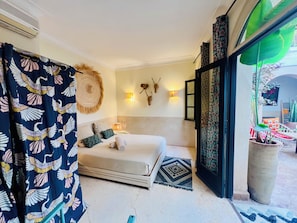 A bedroom with a bed, pillows, a wall-mounted light, decorative wall art, and a view of the outside. - Riad Jeanne 1 (Marrakech)