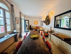 A dining area with a long wooden table, red chairs, a woven placemat, and a wall-mounted light fixture. - Riad Jeanne 1 (Marrakech)