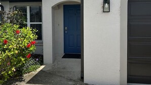En bostadsbyggnad med en blå dörr, en garageport och en liten trädgård med röda blommor.