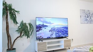 En platt-TV placerad på en vit TV-bänk, med en växt bredvid.