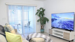 Ett vardagsrum med en soffa, ett tv-appar, en krukväxt och en skjutdörr i glas.