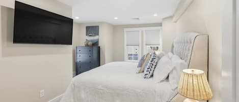 Un dormitorio con cama, cómoda, lámpara y televisor montado en la pared.