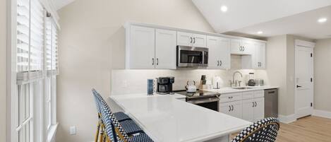 A modern kitchen with white cabinetry, a central island, and a dining area with checkered chairs.