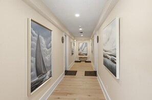 A hallway with artwork on the walls, wooden flooring, and a ceiling with recessed lighting. - LUX on Main | Downtown | Parking | Sleeps 6, #203 (Falmouth)