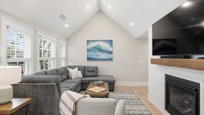 Een moderne woonkamer met een modulaire bank, een flatscreen-tv, een open haard en een groot raam met jaloezieën.