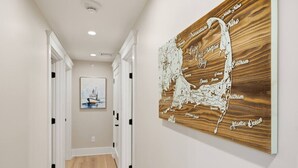 Een gang met een houten kaart van Cape Cod Bay, een inlijsting schilderij van een schip, en witte deuren.