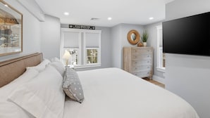 Een slaapkamer met een bed, een dressoir, een spiegel en een televisie.