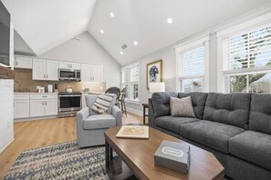 A modern kitchen with white cabinets, a microwave, and a stove. There is a gray sofa and a wooden coffee table in the living area. - LUX on Main | Downtown | Parking | Sleeps 6, #201 (Falmouth)