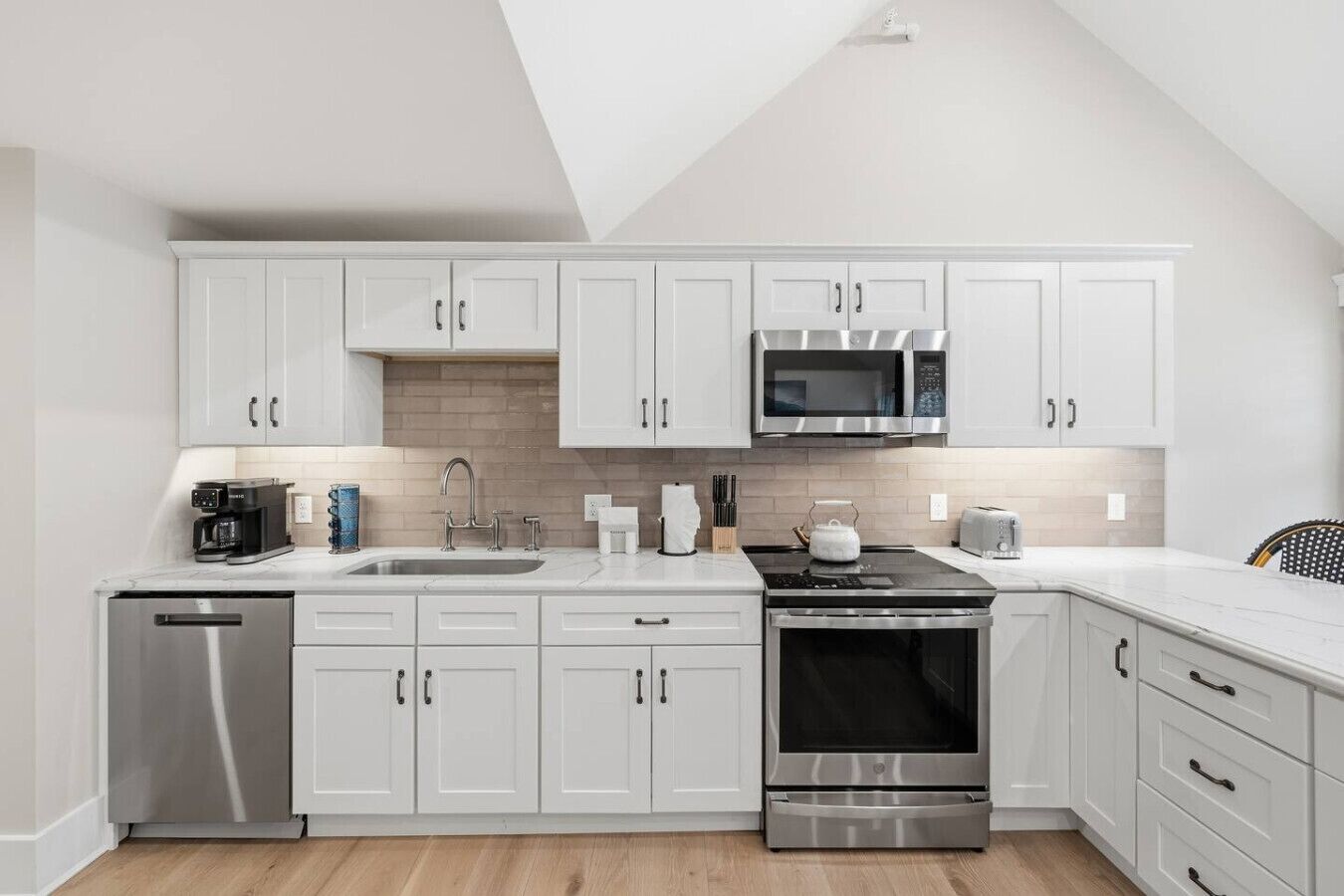 Une cuisine moderne avec des armoires blanches, des appareils en acier inoxydable et un plancher en bois.