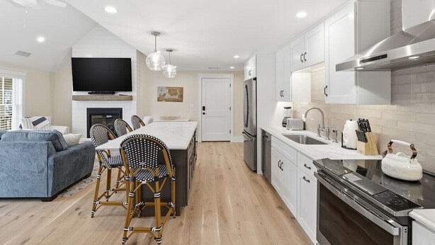 A modern kitchen with white cabinets, a central island, and a dining area with wicker chairs.