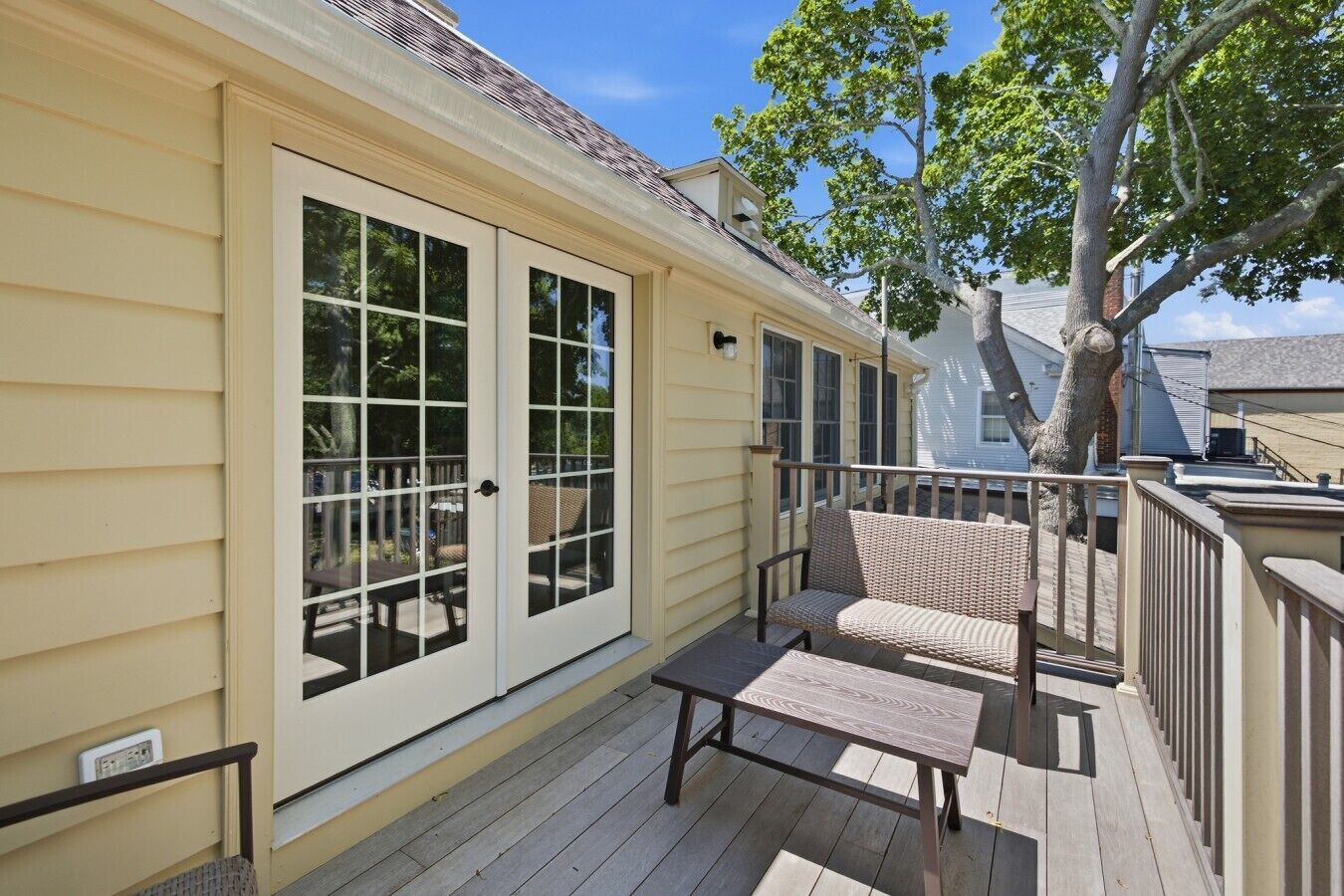 A covered porch with a wooden bench and a door leading to a deck.